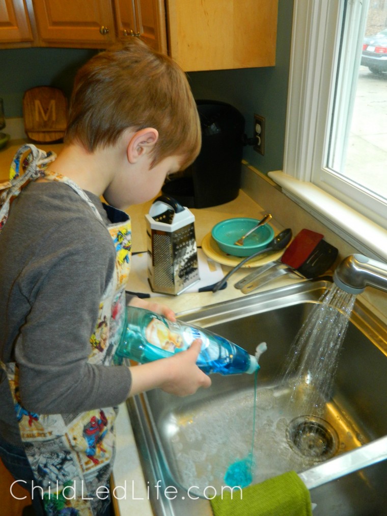 Adding soap for Montessori washing dishes lesson on ChildLedLife.com